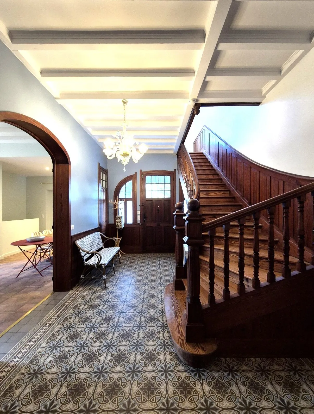Hall d'entrée d'une maison de maître rénovée, carreaux de ciment à frise et escalier bois tournant