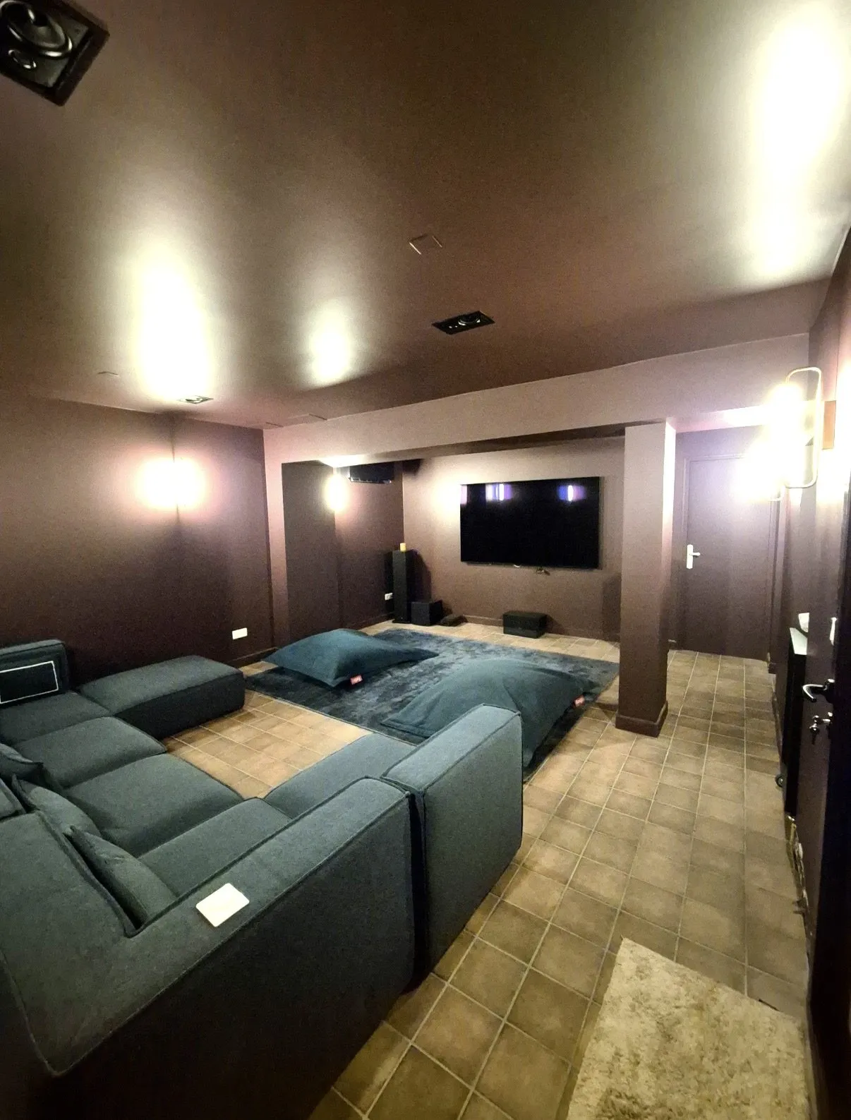 Home cinéma aménagé en sous-sol avec écran mural, banquettes d'angle et éclairage indirect