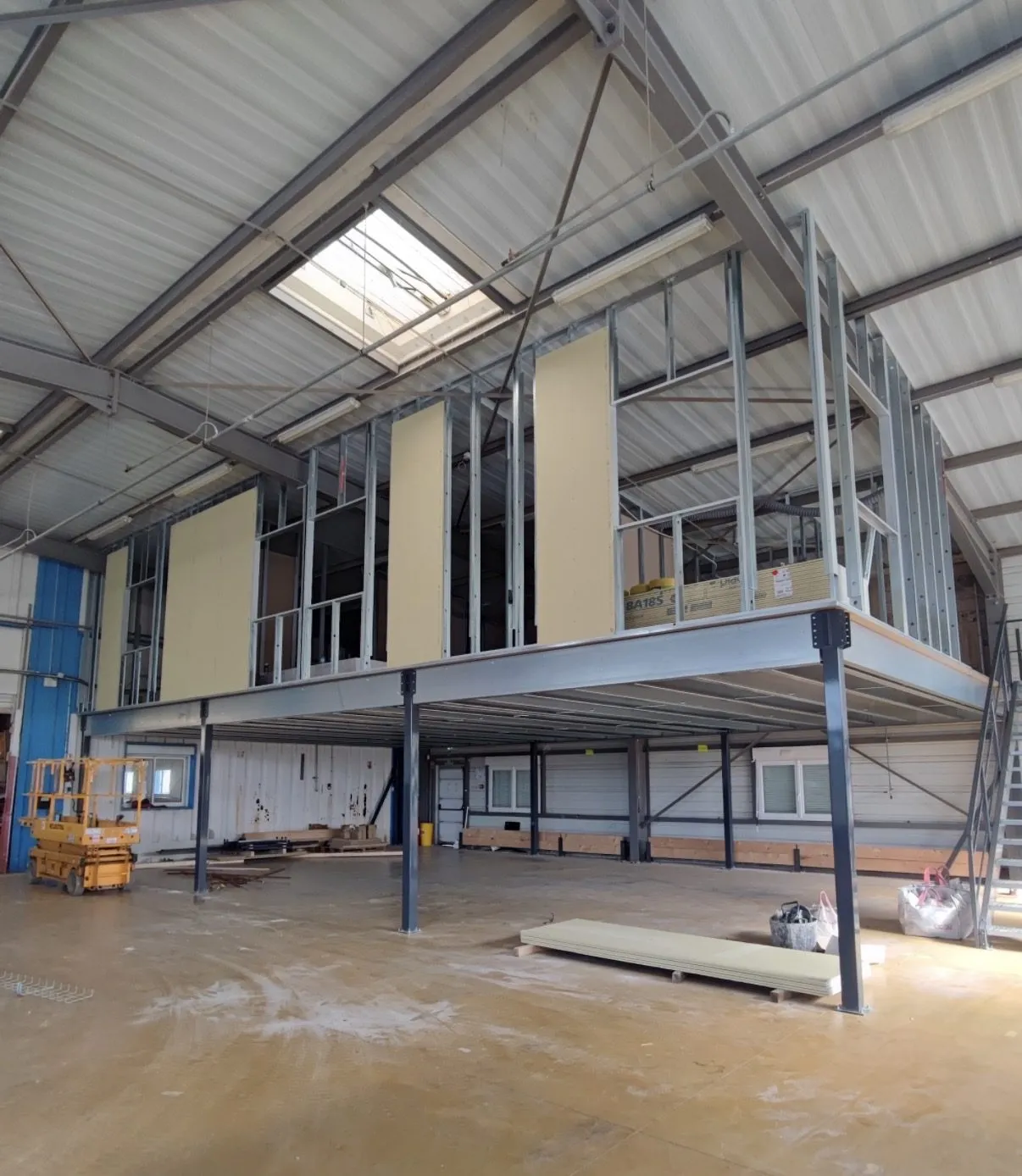 Mezzanine métallique en cours d'habillage dans un bâtiment industriel, ossature montée et premières plaques posées