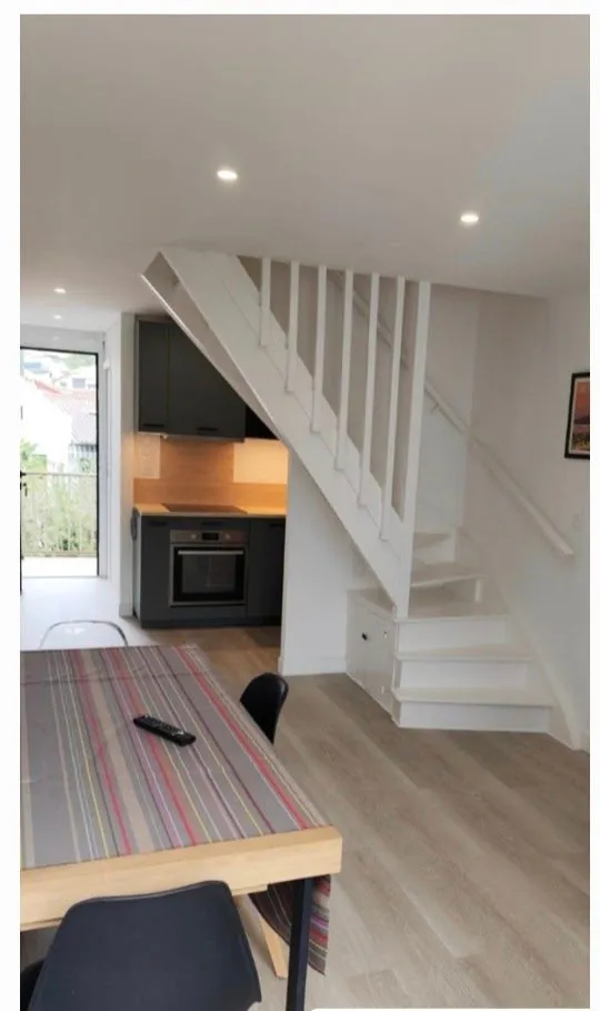 Séjour d'un appartement rénové à Saint-Jean-de-Luz : escalier repeint en blanc, cuisine noire et parquet clair