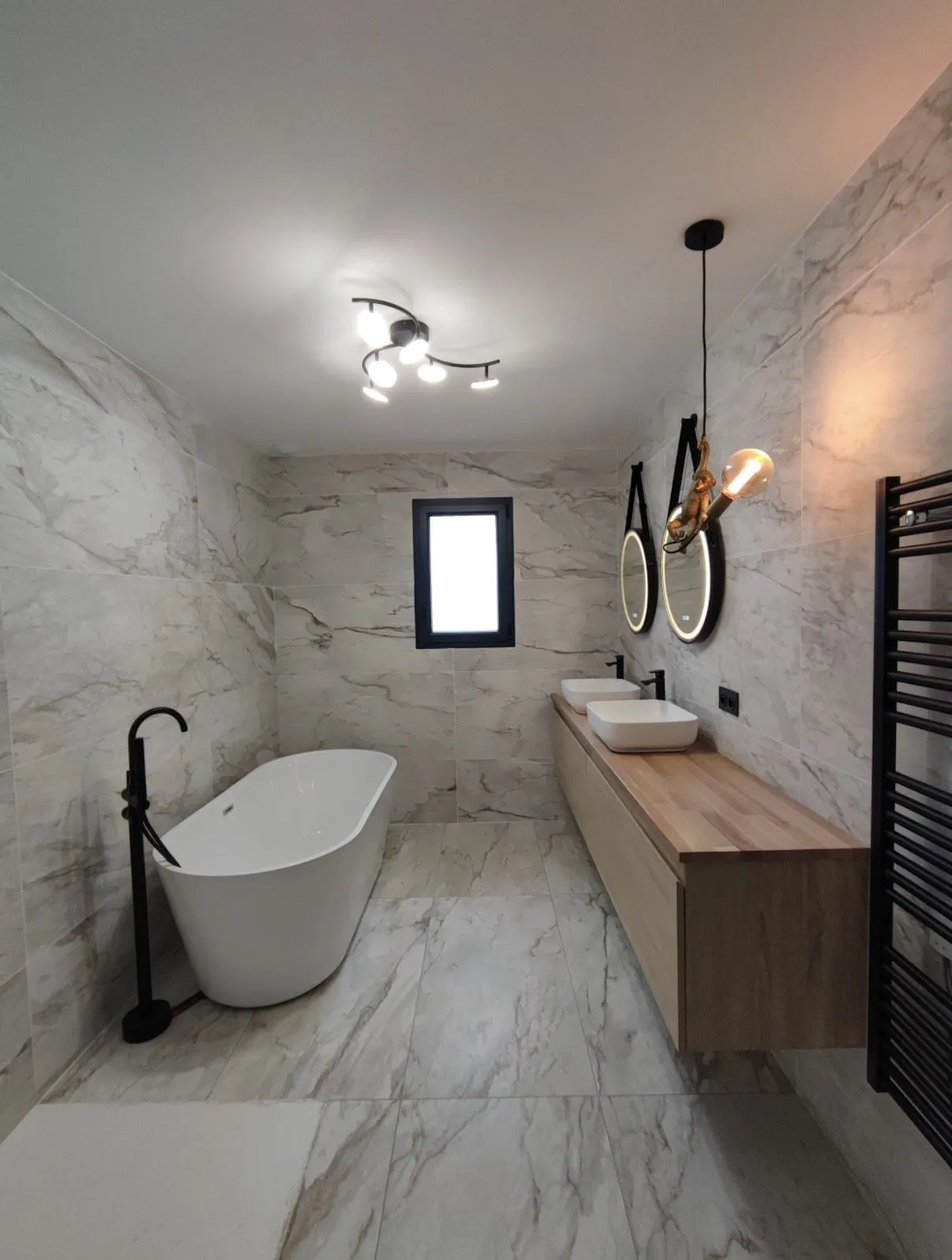 Salle de bains rénovée par JRoux Rénovation : baignoire îlot, carrelage grand format effet marbre et double vasque sur plan chêne