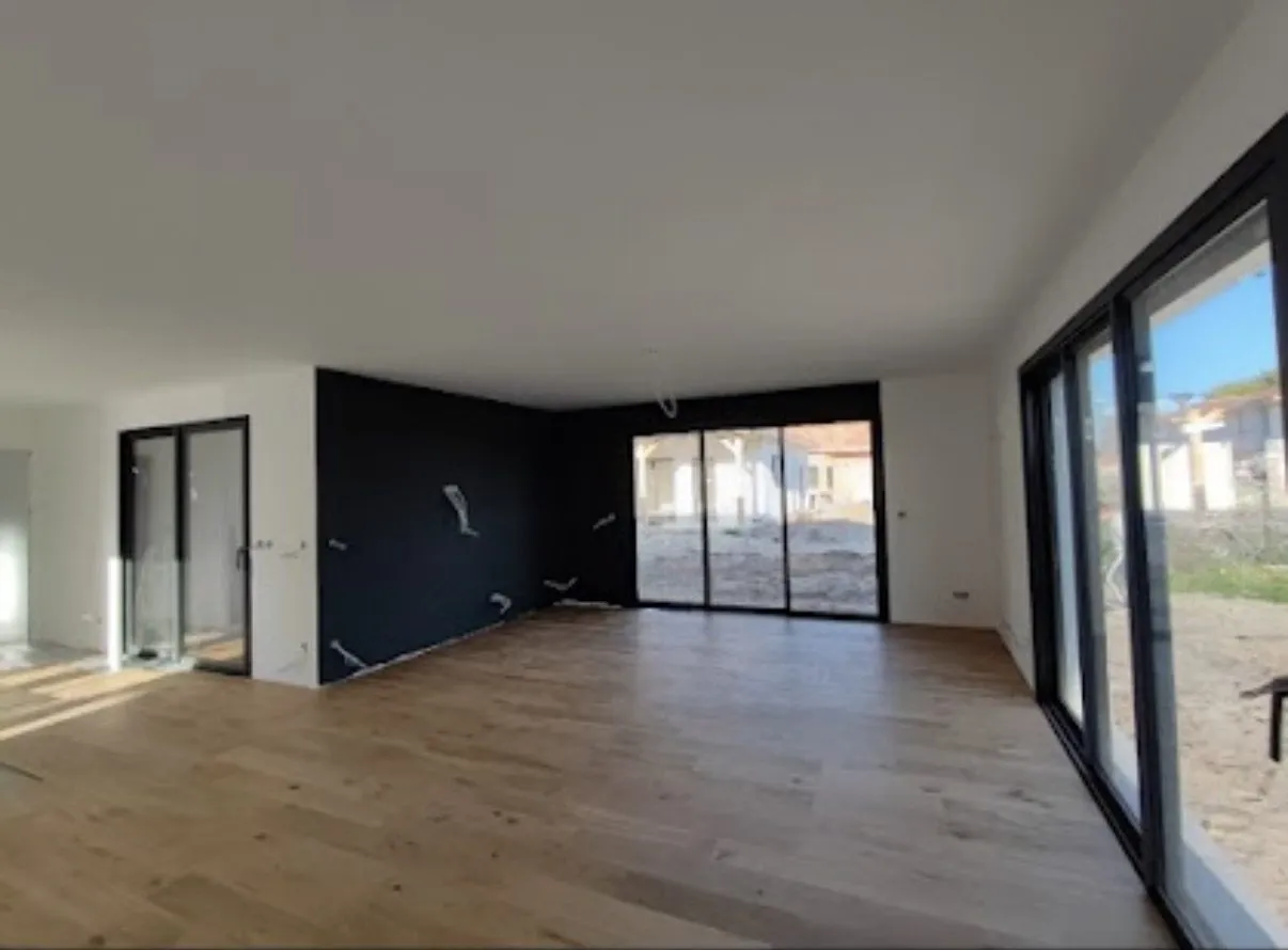 Séjour rénové avec parquet chêne, pan de mur noir et baies vitrées toute hauteur donnant sur le jardin